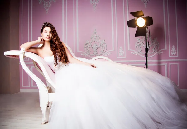 Foto glamourosa de uma bela noiva morena em um vestido de casamento luxuoso deitado no sofá rosa — Fotografia de Stock