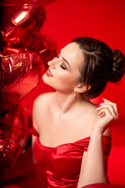 美しいです若いです若いです女性で赤夜ドレス上の赤い背景に大きなハート形の風船 — ストック写真