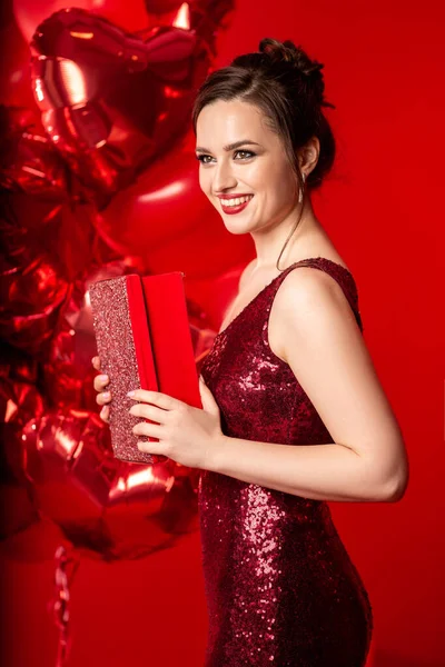 美しいです若いです若いです女性で赤夜ドレス上の赤い背景に大きなハート形の風船 ストックフォト