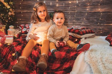 Kız kardeş ve küçük kardeş oturma odasında Noel ağacı ve hediye kutusuyla süslenmiş, ışık rahat bir ortam sağlıyor. Yeni Yıl ve Mutlu Xmas konsepti