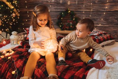Kız kardeş ve küçük kardeş oturma odasında Noel ağacı ve hediye kutusuyla süslenmiş, ışık rahat bir ortam sağlıyor. Yeni Yıl ve Mutlu Xmas konsepti