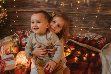 Noel ağacı ve hediye kutusuyla süslenmiş küçük kardeşini oturma odasında tutan kız kardeş, ışık rahat bir atmosfer sağlıyor. Yeni Yıl ve Mutlu Xmas konsepti
