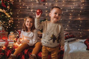 Kız kardeş ve küçük kardeş oturma odasında oynuyor. Noel ağacı ve hediye kutusuyla dekore edilmiş. Işık rahat bir ortam sağlıyor. Yeni Yıl ve Mutlu Xmas konsepti