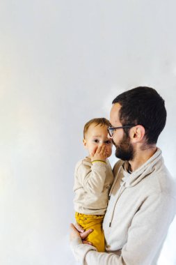Babası, beyaz arka planda ağzını kollarıyla kapatan şaşkın oğluyla birlikte. Baba ve bebek konsepti.