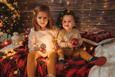 Kız kardeş ve küçük kardeş oturma odasında Noel ağacı ve hediye kutusuyla süslenmiş, ışık rahat bir ortam sağlıyor. Yeni Yıl ve Mutlu Xmas konsepti