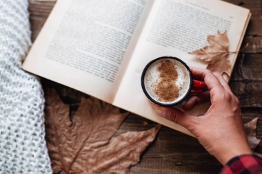 hand of a woman holding cup of coffee while reading a book in autumn