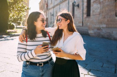 Two women friends visiting an ancient city in spain , Salamanca and holding her mobile phone