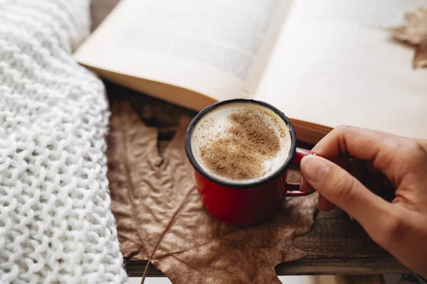Sonbaharda kitap okurken elinde bir fincan kahve tutan kadın.