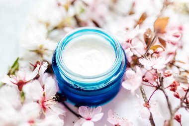 Mavi cam bir kavanozda pembe kiraz çiçekleriyle bitkisel spa kozmetik kremi. Hijyenik cilt losyonu..