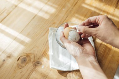 Elinde kürdan olan bir kadının elleri seramik paskalya yumurtasından yumurta kabuğunu çıkarıyor.