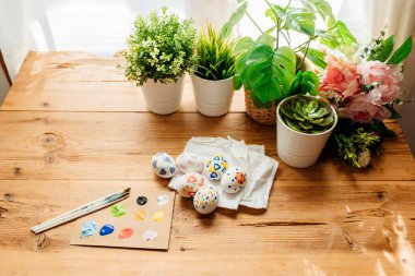 Modern paskalya yumurtalarının düzlüğü boyanmış. Çiçekler ve bitkilerle fırçalar ve boyalar. Ahşap arka planda mutlu paskalya konsepti.