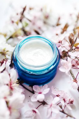 Mavi cam bir kavanozda pembe kiraz çiçekleriyle bitkisel spa kozmetik kremi. Hijyenik cilt losyonu..