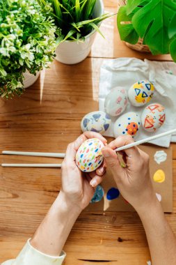 Kadın, el yapımı paskalya yumurtaları boyadı. Çiçekler ve bitkilerle fırçalar ve boyalar. Ahşap arka planda mutlu paskalya konsepti.