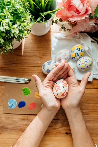 Female holding a modern easter egg. Brushes and paints with flowers and plants. Happy easter concept on a wooden background.