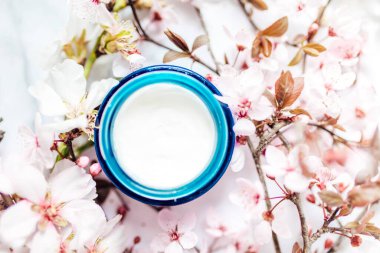 Mavi cam bir kavanozda pembe kiraz çiçekli kozmetik krem manzarası. Hijyenik cilt losyonu..