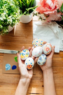Modern bir paskalya yumurtası tutan dişi. Çiçekler ve bitkilerle fırçalar ve boyalar. Ahşap arka planda mutlu paskalya konsepti.