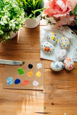 Modern paskalya yumurtalarının düzlüğü boyanmış. Çiçekler ve bitkilerle fırçalar ve boyalar. Ahşap arka planda mutlu paskalya konsepti.