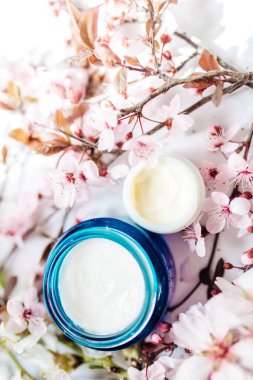 Kozmetik krem ve kapatıcı göz kremleri ve mavi cam bir kavanozda pembe kiraz çiçekleri. Hijyenik cilt losyonu ürünü. Yatay fotoğraf