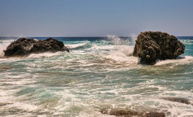 Güzel manzaralı deniz dalgaları su sıçramalarıyla kayalara çarpıyor. Korfu Adası, Yunanistan.