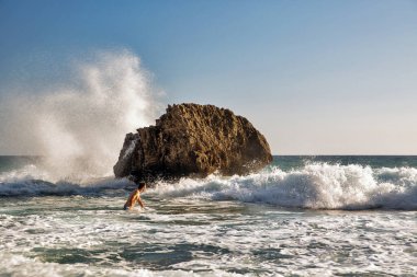 Glyfada, Corfu, Yunanistan - 06 Ağustos 2021: Tanınmayan adam Mirtiotissa sahilinde kayalara çarpan güzel manzaralı dalgalarla denizde yüzüyor.