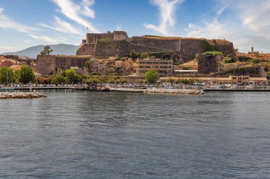 Yeni Kaleli Kerkyra şehri. Korfu adası, Yunanistan. Sakin turkuaz suyu olan deniz koyunda, renkli eski evler, beyaz bulutlu mavi gökyüzü..