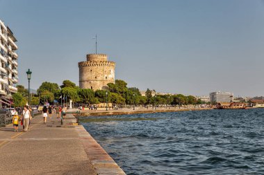 Thessaloniki, Greece - July 27, 2021: Cityscape with people walking along waterfront with bust of Admiral Votsis and White Tower. Thessaloniki is the capital of geographic region of Macedonia.