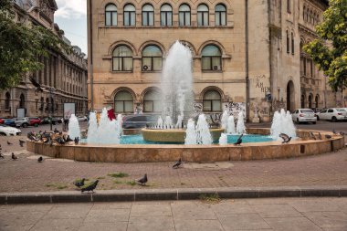 Bükreş, Romanya - 12 Ağustos 2021: Üniversite Meydanı yakınlarında güvercinlerle dolu dekoratif su çeşmesi. Bükreş, Romanya 'nın başkenti ve kültürel, sanayi ve finans merkezidir..