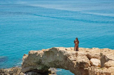 AYIA NAPA, CYPRUS - 24 Mayıs 2021: Kayalık sahil kemerinde duran bikinili güzel genç kadın. Ayia Napa, Kıbrıs 'ın güney kıyılarının uzak doğu ucunda bir turizm beldesi..