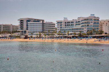 Protaras, Kıbrıs - 25 Mayıs 2021: İnsanlar lüks otellerle deniz kenarında güneşlenip yüzüyorlar. Protaras açık gökyüzü mavi sulara ve kumlu plajlara sahiptir. Bunların en ünlüsü İncir Ağacı Koyu 'dur..