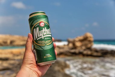 Ayia Napa, Kıbrıs - 29 Mayıs 2021: Beyaz adamın elinde arka planda Ayia Napa tatil beldesi plajı ile birlikte bir kutu Kıbrıs Rum birası bulunuyor.