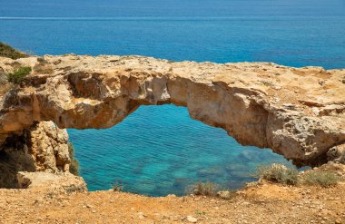 Kıbrıs 'taki Cape Greco yarımadası parkında Aşıklar Köprüsü ya da Kuzgun Kemeri olan deniz manzarası. Ulusal parkı, kaya yolları, turkuaz bir gölü ve doğal bir taş köprüsü olan dağlık bir yarımadadır..