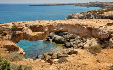 Kıbrıs 'taki Cape Greco yarımadası parkında Aşıklar Köprüsü ya da Kuzgun Kemeri olan deniz manzarası. Ulusal parkı, kaya yolları, turkuaz bir gölü ve doğal bir taş köprüsü olan dağlık bir yarımadadır..