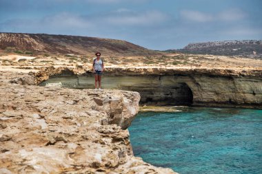 Seascape Cape Greco yarımadası parkında Kıbrıs 'ta bir kadın uçurumun kenarında duruyor. Ulusal parkı, kaya yolları, turkuaz bir gölü ve doğal bir taş köprüsü olan dağlık bir yarımadadır..