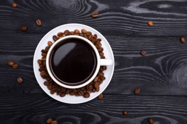 Kahve fincanının en üst görüntüsü siyah ahşap masada kahve çekirdeklerini sarmıştı.