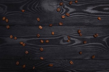 Kavrulmuş kahve çekirdekleri siyah desenli ahşap masaya saçılmış.