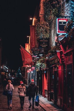 DUBLIN, IRELAND, 24 ARALIK 2018: Tapınak Bar tarihi bölgesinde yürüyen insanlar, canlı gece hayatı olan kültürel bir semt. Barın gece manzarası, ışıklarla dolu ve tipik İrlanda barı..