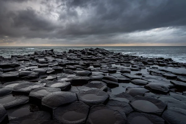 Kuzey İrlanda 'da dramatik bulutlu gökyüzü ile bir dönüm noktası olan Giants Causeway adlı kıyıdaki doğal altıgen taşlar.