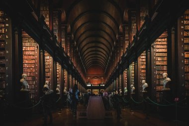 DUBLIN, IRELAND, 21 ARALIK 2018: The Long Room in the Trinity College Library, home of Kells. Büyük miktarda kitap ve sandık heykeliyle mekânın perspektifi.