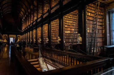 DUBLIN, IRELAND, 21 ARALIK 2018: The Long Room in the Trinity College Library, home of Kells. Büyük miktarda kitap ve sandık heykeliyle mekânın perspektifi.