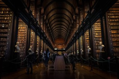DUBLIN, IRELAND, 21 ARALIK 2018: The Long Room in the Trinity College Library, home of Kells. Büyük miktarda kitap ve sandık heykeliyle mekânın perspektifi..