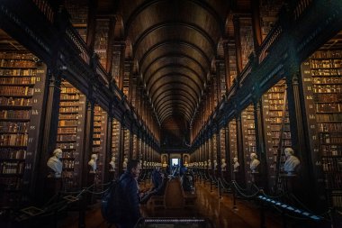 DUBLIN, IRELAND, 21 ARALIK 2018: The Long Room in the Trinity College Library, home of Kells. Büyük miktarda kitap ve sandık heykeliyle mekânın perspektifi..