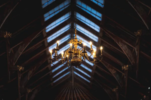 Krásný osvícený zlatý lustr visící pod rozmazaným stropem, plný detailů se soškou s trumpetami. — Stock fotografie