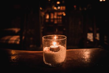Karanlık bir sahneyi aydınlatan bir bardağın içinde izole edilmiş bir gece ve ahşap bir masa ve güzel bir arka plan yansımaları.