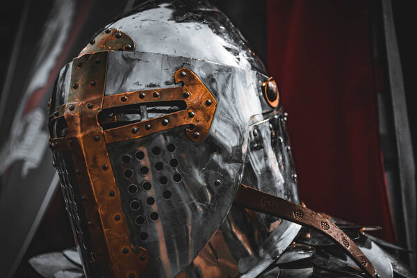 Shiny silver medieval iron knight helmet with a golden cross, full of scratches due to battles.