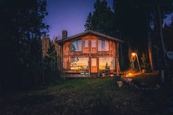 BARILOCHE, ARGENTINA, 19 DE JUNIO DE 2019: Exterior de una acogedora y relajante cabaña de madera en el bosque durante los últimos momentos de luz con puesta de sol reflejada en sus ventanas. — Foto de Stock