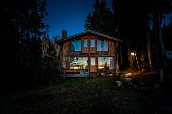 BARILOCHE, ARGENTINA, JUNE 19, 2019: Exterior of a wooden cozy and relaxing cabin in the forest during the last moments of light with sunset reflecting on its windows. — Stock Photo, Image