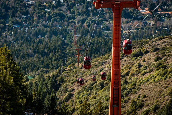 Arka planda dağların zirvesine giden yolcuları taşıyan kırmızı teleferiklerin manzarası. — Stok fotoğraf