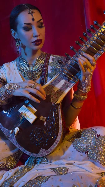 Beautiful young indian woman in traditional Sari clothing with Oriental Jewelry Playing the Sitar. Indian woman Playing night Raga the Sitar, Eastern Music. Musical Candlelight Party in India.