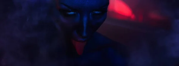 Halloween Horror night: goddess of destruction Kali. Female eyes and mouth with bloody tongue. Young vamp Woman showing red tongue. On the background of dark blue smoke and sunset