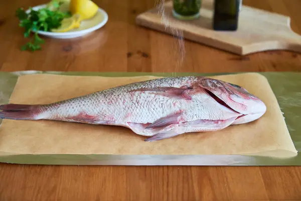 Dorado balığını zeytinyağı ve bitkilerle pişirme işlemi. Kadın eli, yakın plan. Ev yapımı yemek kavramı, aşçılık hobisi.
